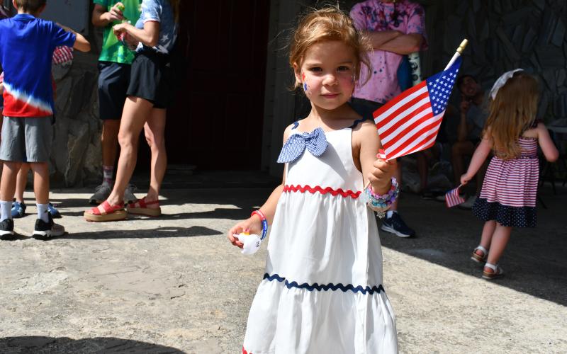 Megan Horn/The Clayton Tribune. Claudette Sagraves waves an American flag in a red, white and blue dress after getting her face painted in Sky Valley on Friday, July 3.