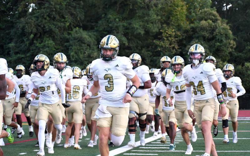 Wesley Branch/The Clayton Tribune. Rabun Gap’s Grayson Clary (center) runs onto the field with his team ahead of Rabun Gap’s game versus Providence Day last season. After transferring to RGNS last year and splitting time with 2026 graduate Gavin Owens, Clary will be Rabun Gap’s starting quarterback this season.