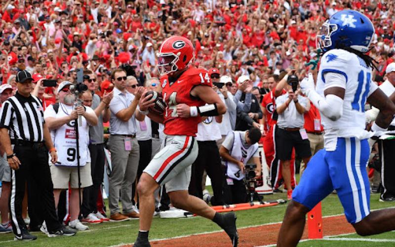 Wesley Branch/The Clayton Tribune. With former UGA quarterback Jake Fromm (far left) clapping, Gunner Stockton runs into the end zone for a touchdown against Kentucky in Sanford Stadium on Oct. 4, 2025.