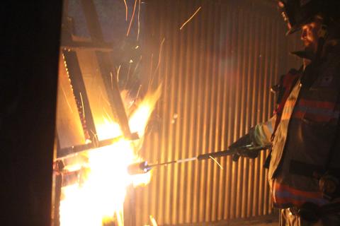 Megan Broome/The Clayton Tribune. Jerry Buice lights a pile of wood on fire inside a metal building used for firefighter training at the Rabun County Fire Services training center at Station 4 in Lakemont.