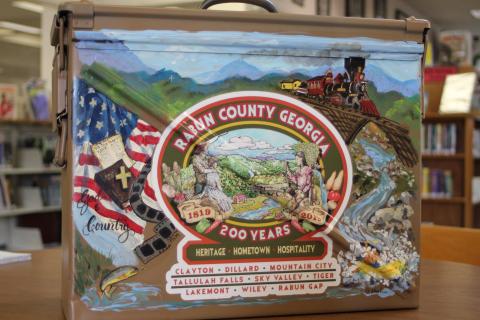 Megan Broome/The Clayton Tribune. The time capsule that will be buried for the Rabun County Bicentennial and opened in 100 years was painted by local artist Diane Rush. The time capsule is a military ammo box that was donated by Alan Price. 