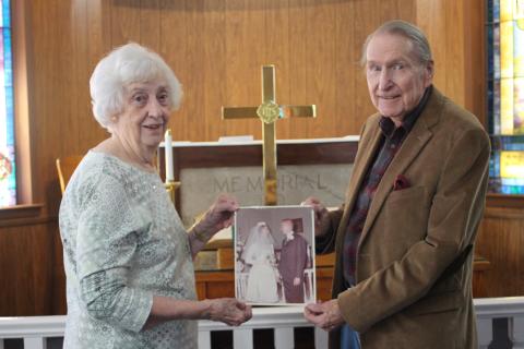 Megan Broome/The Clayton Tribune Catherine Turpen and Rev. James E. Turpen, Sr. stand in front of the altar at Tallulah Falls United Methodist Church and hold a picture from their wedding day where they said “I do” in the same spot  55 years ago on Dec. 20, 1964. 