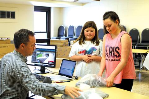 Megan Broome/The Clayton Tribune. Greg Purcell, technology director for Rabun County Schools, hands out Chromebooks to fifth grader Nevaeh Fain and sixth grader Hanby Denning during distribution at the Board of Education Office on Tuesday. The Chromebooks will allow students to complete online learning while students are out of school due to COVID-19. 