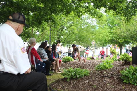 Megan Broome/The Clayton Tribune. Mickey Wood, left, and Francesca Franklin, along with members of the community watch as Dominic Cross places flags at the Veterans’ Monument in front of the Rabun County Courthouse as the names of all those in the armed forces who have passed away in the last year were read aloud. 
