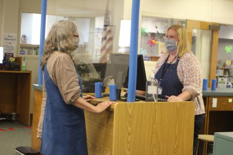 Megan Broome/The Clayton Tribune. Peggie Wilcox, circulation clerk, left, and Melissa Poslusny, senior clerk, demonstrate checkout procedures amidst the library's new contact precautions during the soft reopening of the Rabun County Library after being closed due to COVID-19. 