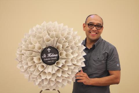 Megan Broome/The Clayton Tribune. Father Pedro Poloche holds up a wreath made by a parishioner at St. Helena Catholic Church. The wreath is made out of church bulletins that Poloche saved to write down the names of every family in the congregation to remember to pray for them during times of hardship. Each bulletin represents a different family name. 