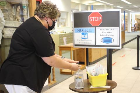 Megan Broome/The Clayton Tribune. The Rabun County Public Library reopened on Tuesday and patrons are required to wear masks while browsing and follow other health guidelines like sanitizing hands and following the direction arrows to maintain a six-foot distance.  Jennifer Buchanan, circulation supervisor, uses hand sanitizer to demonstrate measures patrons are asked to take upon entering the library. 