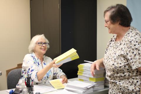 Megan Broome/The Clayton Tribune. Elaine Lawson, absentee ballot clerk for the Rabun County Board of Elections Office, right, hands a stack of completed absentee ballots to poll worker Ann D’Agostino for processing at the Board of Elections Office Tuesday. 
