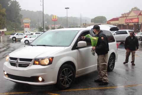Megan Broome/The Clayton Tribune. Rabun County Detention Center Officer Daniel Nicholson hands out flowers and chocolate to families during the Faith and Blue food distribution event last Saturday. Each family was given these along with boxes of food. 