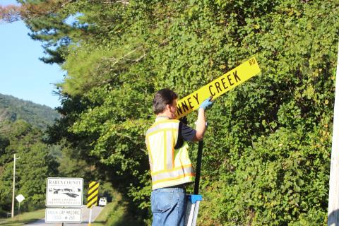 Megan Broome/The Clayton Tribune. Keith Yunger, sign technician for the Rabun County mapping department, replaces one of the road name signs located on Warwoman Rd. that was stolen on Labor Day weekend.
