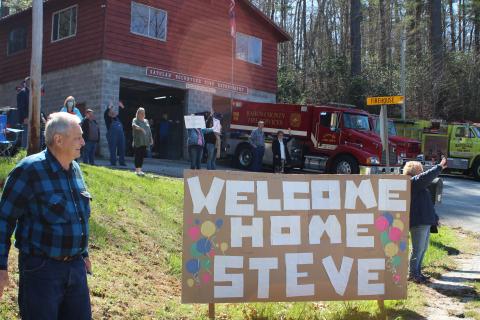 Megan Broome/The Clayton Tribune. Friends and family of former Satolah Fire Department Chief Steve Wilson gathered at the Satolah Fire Station Tuesday to welcome him home after a months-long battle being hospitalized with COVID-19. Jimmy Nix stands beside the homemade sign and cheers for Wilson along with other friends and family members. 