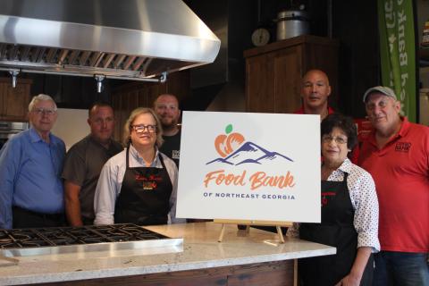 Megan Broome/The Clayton Tribune. Representatives from area food banks attended an unveiling of the new Food Bank of Northeast Georgia logo in the Food Bank Teaching Kitchen last week. Richard Boone, left, Aaron Holt, Laura Hunter, Philip Wilkes, James Brim, director of the Food Bank Mountain Branch, Joanna Baumgartner and Dave Smith stand in front of the new logo after it is revealed. 