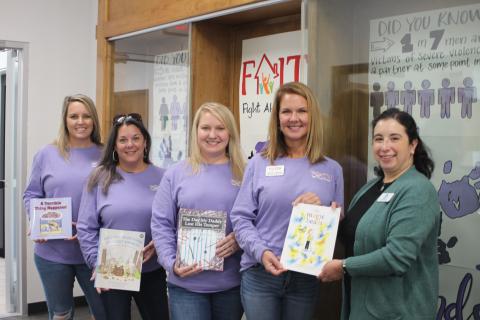 Megan Broome/The Clayton Tribune.  Brooke Cannon, grant administrator, left, Laura Davis, Empowering Families coordinator, Kayla Talley, FAITH legal advocate, Monica Blalock, director of community awareness, present books to Dyana Costello Banks, library manager, for donation to the Rabun County Public Library, in front of the library display. 