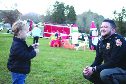 Megan Broome/The Clayton Tribune. Jaxon Golden, left, laughs and talks with Dillard Police Chief Jeremy Parker while eating a S’More at the “A Night Out in Christmastown” event held in Dillard Dec. 8. 