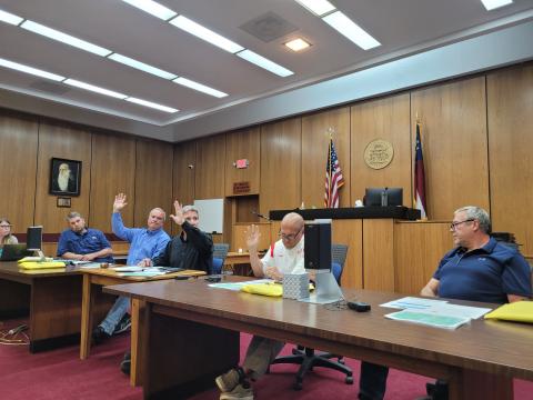 Megan Broome/The Clayton Tribune. A rezoning request for a 20.15 acre property off of Highway 76 East from Agricultural (A) to Commercial Business (CB) for the purpose of building storage units was denied by Commissioners in a 3-2 vote at Tuesday’s meeting. Kent Woerner, Greg James and Scott Crane show their hands in favor of the motion to deny the rezoning, while Will Nichols and Tom Garrison voted in opposition to the motion. 