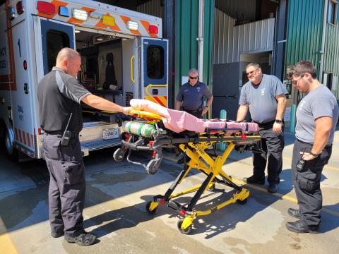 Megan Broome/The Clayton Tribune. Rabun County EMS Captain Trampes Stancil, EMS/911 Director Mike Carnes; Paramedic Don White and EMT Will Shanks demonstrate how the Stryker Power Load System automatic hydraulic lifting equipment lifts patients who are on stretchers in and out of the ambulance. This system significantly helps reduce workplace injuries.