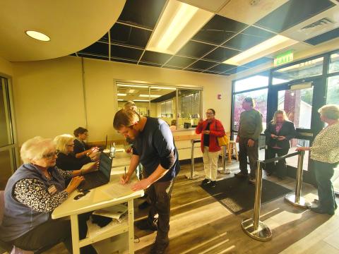 Megan Broome/The Clayton Tribune. The line of voters waiting to check in to cast their ballots extended outside of the elections office Tuesday afternoon 30 minutes before polls closed. In the forefront, poll worker Ann D’Agostino checks-in voter Caleb Watson as poll workers Sandra Wood and Kay Townsend also check in other voters. To the right, poll worker Jane Thomason helps assist voters through the process. 