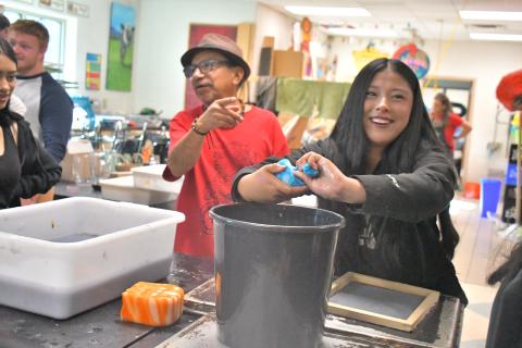 Megan Broome/The Clayton Tribune. Student Camila Gaspar smiles as she hand makes paper with guest artist Javier Silverio onlooking in the Rabun County High School art room April 21. Gaspar squeezes a sponge to make paper just as Silverio does at Taller Leñateros in Chiapas, Mexico.