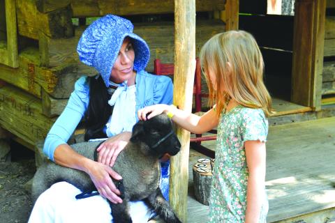 Enoch Autry/The Clayton Tribune. The annual Heritage Days event returned on June 9 and 10 at the Foxfire Museum and Heritage Center. Pictured, Stephanie Branch talks with Ally St. German as the 6-year-old pets “Hampshire” the lamb. Left: Enoch Autry/The Clayton Tribune. Sisters Anna, 7, and Claire, 4, Miller play inside one of the small Foxfire structures that were built for children.