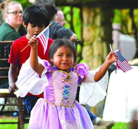 Megan Broome/The Clayton Tribune. Annalia Contreras, 3, waves American Flags in excitement and passes them out to visitors to The Dillard House for the Memorial Day weekend event on the Oaklawn Sunday, May 28. Behind her is her big brother Mateo Contreras, 6. 