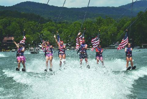 Enoch Autry/The Clayton Tribune. Members of the Ski Patriots wave toward people on balconies of houses on Lake Burton on July 1. In groups, the skiers went around the Rabun County lake for a total of 27 miles. This popular annual event has been putting smiles on individuals’ faces for the past 15 years. This time the youngest skier was 10 years old.