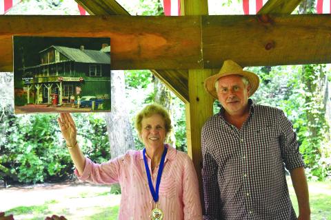 Enoch Autry/The Clayton Tribune. Helen Swain shows her award-winning painting, “Alleys Store 1964,” while standing next to Callaway. Below: James Fairchild of Tiger plays the accordion during the Great American Art Show & Contest on Aug. 5 in Lakemont. In the background are hanging white umbrellas. Other umbrellas were hung around the park area.