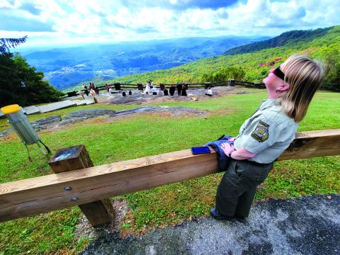 Enoch Autry/The Clayton Tribune. Jessica James-Weeks, the manager of Black Rock Mountain State Park, gazes toward the sky while wearing her special glasses to view the solar eclipse on Oct. 14. In the background, Garrett McClure and Taylor Herrington say their vows in the Blue Ridge Mountains.