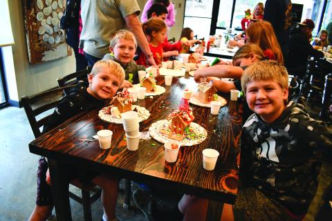 Megan Horn/The Clayton Tribune. Parker Cavender, 10; Easton Cavender, 8; and Holden Cavender, 6, smile as they display their decorated gingerbread houses at the Food Bank Teaching Kitchen event Dec. 13. 