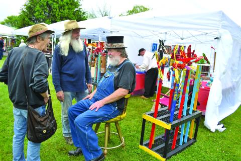Enoch Autry/The Clayton Tribune. Dinglerfest “Episode 2” to the benefit Sid Weber Memorial Cancer Fund offers plenty of visuals at the R.M. Distillery in Dillard on May 4 as folk artists and visitors dodged rain showers deposited from a day of dark clouds. ABOVE: Pat Garner and Randy Wood talk with event organizer Charlie Dingler. Left: John Harrison has to do double take at the bagpipe-playing dinosaur artist Daniel Bollinger.