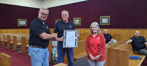 Megan Horn/The Clayton Tribune. Commissioner Kent Woerner, left, presents a Resolution to Andy and Deborah Hunter honoring them for the over 40 years of service that Andy’s Market gave to the community during the May 28 commission meeting. The local grocery store recently closed after decades. 