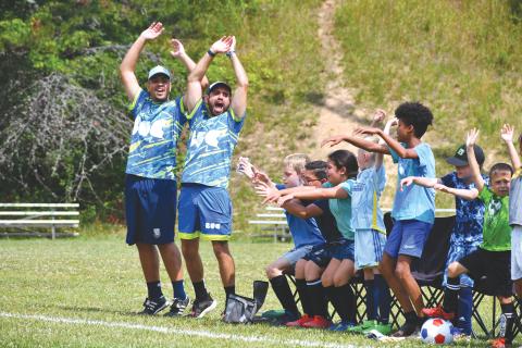 Wade Cheek/The Clayton Tribune. BUC soccer coaches Lucas Padilha and Gabriel Resende celebrate and cheer with local Rabun County kids after a goal during last week’s Brazilian United soccer camp that was held at the Rabun County Recreation Department from June 17-21. ABOVE RIGHT: BUC coach Nathan Nascimente dribbles the ball through youth defenders at this summer’s camp at the Rabun County Recreation Department. The five-day camp allowed campers to learn soccer skills while also having fun with experienced 