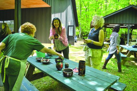 Enoch Autry/The Clayton Tribune. Kristin Mueller of Atlanta proudly shows her pottery to her sister Karin Mueller (right) at the Hambidge Center open house event on May 11. The U-Do-Raku activity was popular as pots were glazed and fired. Left: Christie Lyons and 13-year-old daughter Tricia Lyons of Lawrenceville work on their pottery at the open house. Tricia attends Hudgens Art School in Duluth. 