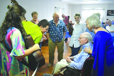 Enoch Autry/The Clayton Tribune. With Laura Chastain standing behind him, 101-year-old Ervin Chastain talks with Bluegrass and Company band members Alyssa White, Elijah Ellenburg and Malachi Ellenburg, and also Beth and Jack Knight at a June 15 birthday celebration at Battle Branch Baptist Church. 