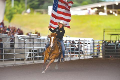Wade Cheek/The Clayton Tribune. Jamie Ellsworth, a breakaway roper, makes her rounds with the American Flag at Rabun Arena as part of the opening ceremonies of last weekend’s Bar W Rodeo that started on Friday, July 5.