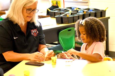 Enoch Autry/The Clayton Tribune. Superintendent Dr. April Childers assists kindergartener Emersyn Fuller with her clay on the first day of school on Tuesday, Aug. 6. Below: School Resource Deputy Sgt. Lindsey Owens directs school traffic on the first day Tuesday, Aug. 6. 
