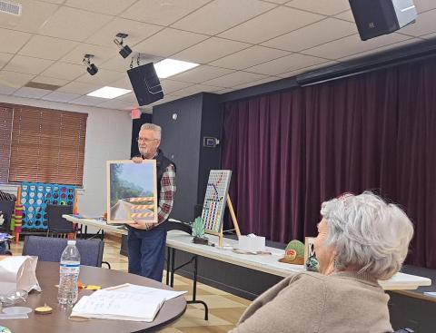 Megan Horn/The Clayton Tribune. Lewis Hinely showcases his artwork at the North Georgia Arts Guild members’ Show and Tell on Oct. 17. Hinely talked about how detours in artwork can be inspired by real life with this painting of a road detour sign. Guild member Kathy Ford is pictured in the forefront. Below:  Joey Aldrich-Burel presents her painting in pastels that was inspired by Vincent Van Gogh.