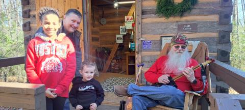 Megan Horn/The Clayton Tribune. Les Barnett of Mountain Man Music, right, demonstrates his panjo and canjo creations at Gott Cabin during “A Foxfire Christmas” on Dec. 7. Chris Adams, Kylee Curtis, 9, and Matthew Curtis, 3, learn a lot about instrument making from Barnett. 