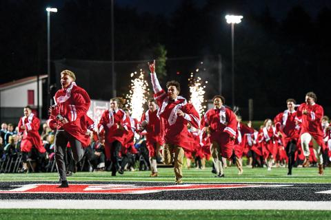 Wade Cheek/The Clayton Tribune. As sparks fly, the Rabun County High School Class of 2025 races to the victory bell at Frank Snyder Memorial Stadium, celebrating their completion of high school. 