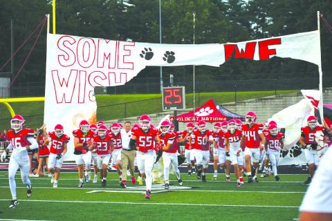 Enoch Autry/The Clayton Tribune. The Rabun County cheerleaders continued their tradition of creating special banners for each Wildcat football game so the team can run through them onto the football field. Here the players and first-year head coach Rance Gillespie (left center) make their way toward the home sideline during pregame of the Aug. 8 scrimmage against visiting Franklin, N.C. 
