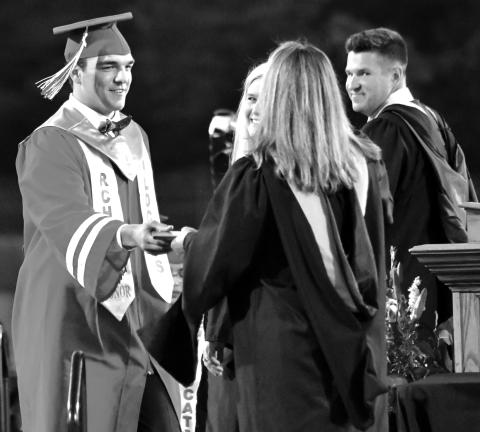 Enoch Autry/The Clayton Tribune. Rabun County High School Principal Justin Spillers (far right) and then Superintendent Dr. April Childers smile as Class of 2022 honor graduate and record-setting Wildcat quarterback Gunner Stockton receives his diploma in May 2022 from his mother Sherrie Stockton, then a RCHS counselor. 