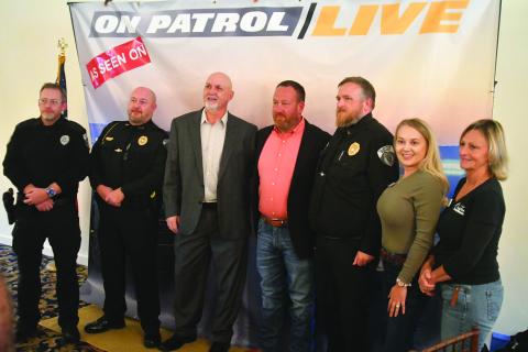 Enoch Autry/The Clayton Tribune. Clayton police officers and Clayton council members and staff pose for a photograph with Hazen (Ark.) Police Chief Bradley Taylor (center) during his Oct. 17 visit to Rabun County as part of the Rabun County Chamber of Commerce Business Breakfast. Taylor is a regular on the television show “On Patrol: Live.”