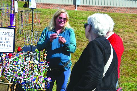 Enoch Autry/The Clayton Tribune. Danette Peters (center) of Why Knot Designs of Blairsville, Ga., talks with customers at the Nov. 1 Of These Mountains Fall MarketPlace on the Rabun County Civic Center Pavilions property. Why Knot Designs was one of the 120 booths that set a record for vendors at the event at the height of “Leaf Season.”
