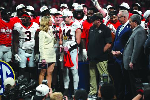 Keith Barlow/CNI News Service. Holding his MVP trophy with his teammates and head coach Kirby Smart on the stage with him, Georgia quarterback Gunner Stockton answers questions from Laura Rutledge after the Bulldogs’ 28-7 win.