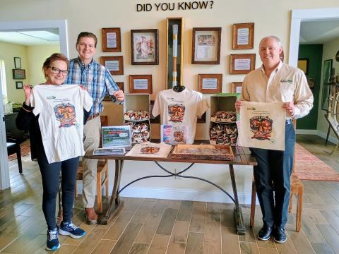 Megan Horn/The Clayton Tribune. The Rabun County Welcome Center has plenty of swag for sale as part of America’s 250th birthday celebration including challenge coins commemorating 250 years, canvas tote bags and t-shirts. Pictured holding the merchandise are Welcome Center Manager Linda Scofield, left; Mickey Duvall, business and economic development strategist; and Rick Story, Rick Story, president of Forward Rabun/Rabun County Chamber of Commerce. 