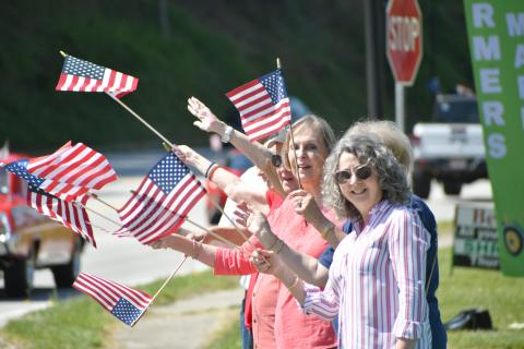 Enoch Autry/The Clayton Tribune. A group of patriotic residents wave American flags at the passing convoy on the Highway 441 sidewalk near the Food Bank of Northeast Georgia.