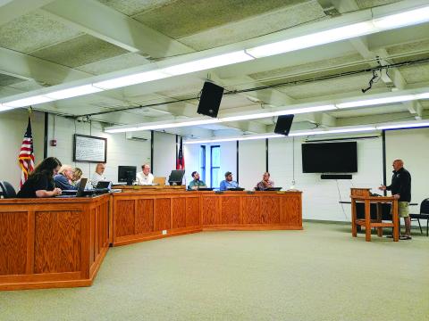 Megan Horn/The Clayton Tribune. Moonrise Distillery owner Doug Nassaur, far right, talks to Clayton City Council members on July 14 about delinquent taxes reported by the city. Nassaur addresses (from left) City Manager Kessiah Gipson, Council Member Tony Allen, City Manager Trudy Crunkleton, Mayor Roy Quilliams, City Attorney Mitch Baker, and council members Colt Woodall, Channing Watts and Stacy Fountain. 
