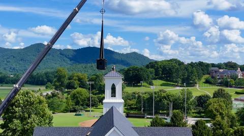 Photo courtesy Scott Poss.  A crane from TKS Installation and Sales of Warner Robins, Ga., lifts the new steeple and spire to the belfry tower of the new sanctuary of Rabun Gap Presbyterian Church. Chuck Lanier perches atop the tower to guide it in place. In the background is the Rabun Gap Nacoochee School, where the church first met in 1929.  