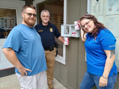Megan Horn/The Clayton Tribune. Nic Huber, Peer Support Specialist for Unite RABUN, left; Sky Valley Police Department Lt. David Edwards; and Unite RABUN Executive Director and Peer Support Specialist Brittany Roquemore install an “Overdose Emergency Kit” equipped with Naloxone at Sky Valley City Hall on Oct. 5. They installed six kits at five different locations in the City of Sky Valley. 
