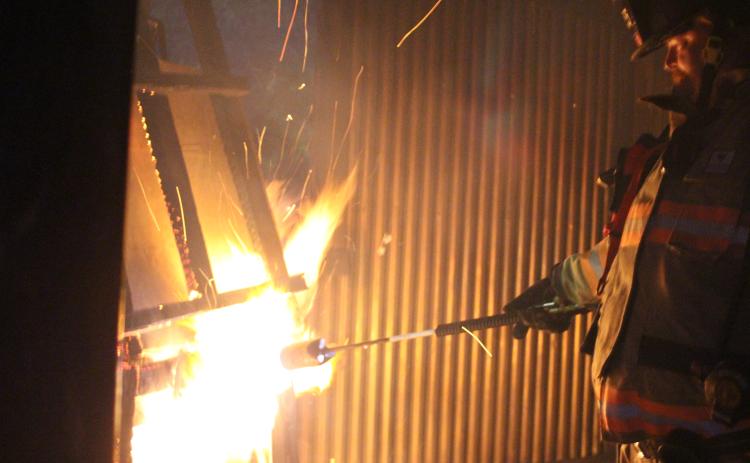 Megan Broome/The Clayton Tribune. Jerry Buice lights a pile of wood on fire inside a metal building used for firefighter training at the Rabun County Fire Services training center at Station 4 in Lakemont.