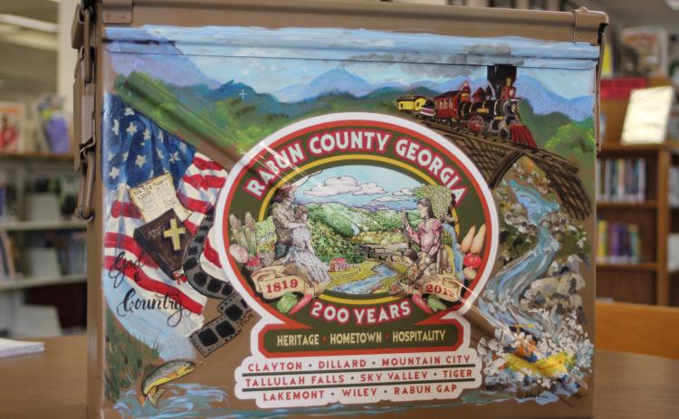 Megan Broome/The Clayton Tribune. The time capsule that will be buried for the Rabun County Bicentennial and opened in 100 years was painted by local artist Diane Rush. The time capsule is a military ammo box that was donated by Alan Price.